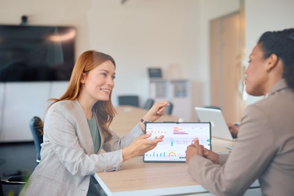 zwei Personen an einem Tisch, ein Tablet, auf dem Diagramme zu sehen sind